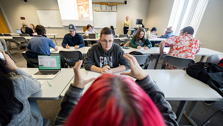 Students in Dr. Chelsea Davis' world history class discuss and draw an image of WWII propaganda on the screen at the front of the class.