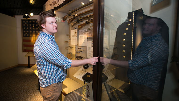 A history student looks into a case displaying a civil war uniform during his internship at Wilson's Creek National Battlefield