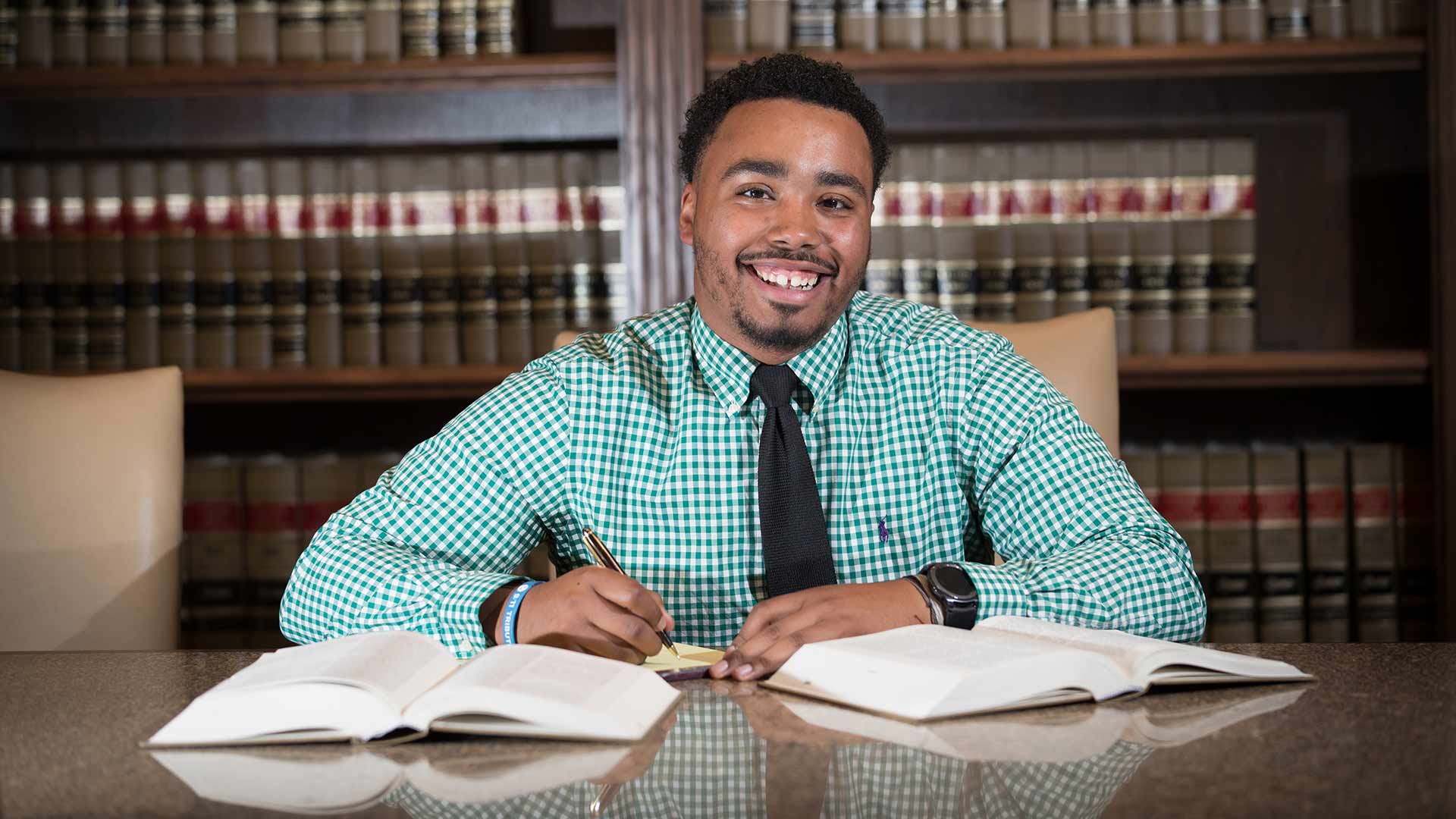 A pre-law student looks up to smile while taking notes from two big textbooks.