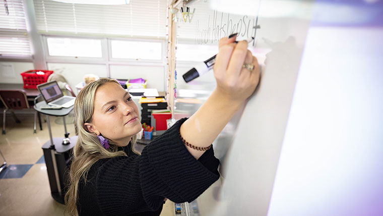 Grace Mudd writes on the whiteboard in her classroom at Cherokee Middle School.