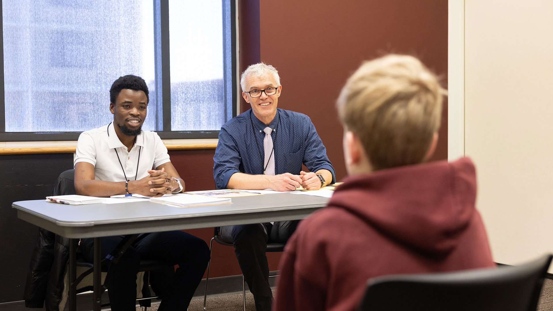 Two judges sit behind a table as they chat with a student on National History Day.