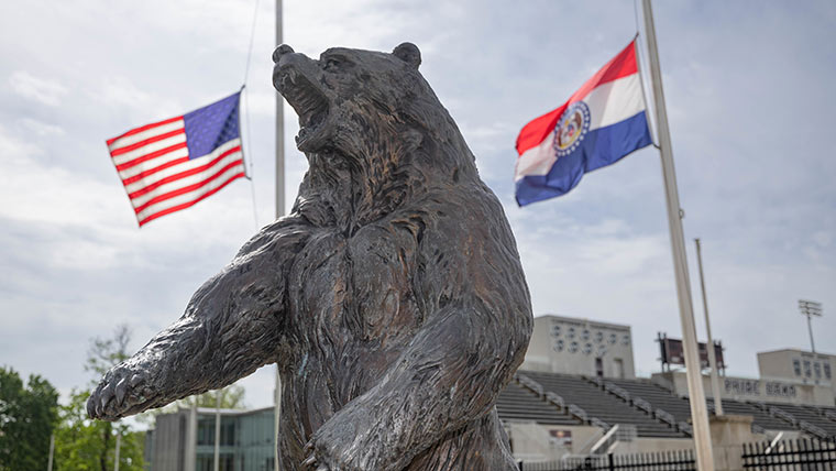 A large bear statute with the USA and Missouri Flags waving in the background.